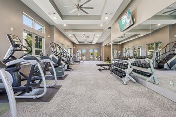 A spacious gym with treadmills, elliptical machines, and a ceiling fan.